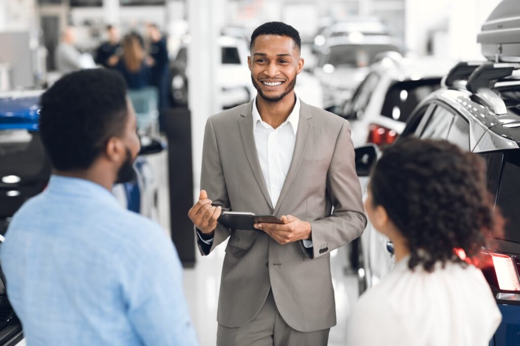 Salesman In Car Dealership Talking With Customers Helping Choose Auto